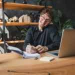 Företagare pratar i telefon och antecknar vid sin laptop