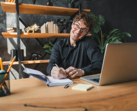Företagare pratar i telefon och antecknar vid sin laptop
